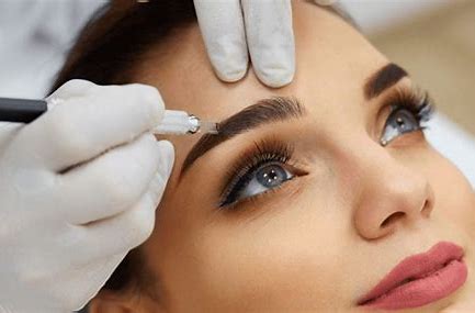 A close-up image of a woman receiving permanent makeup treatment on her eyebrows, with a technician using a tool while wearing gloves.