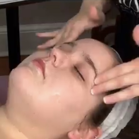 A person receiving a facial treatment in a spa setting, with a hand gently massaging their forehead.